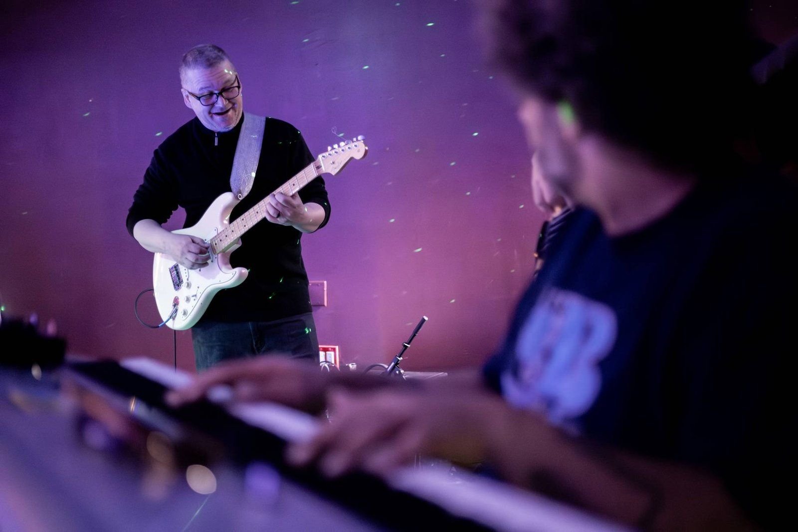 Keyboardist and guitarist performing under purple stage lights